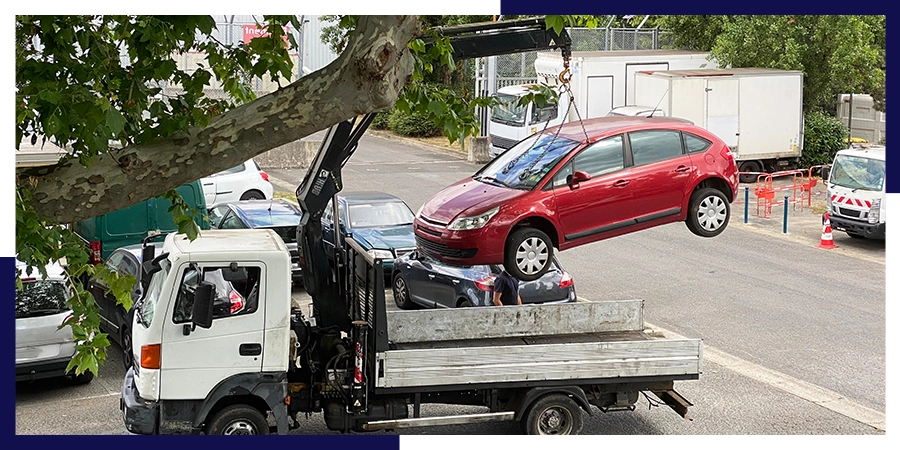 Épaviste et ferrailleur Narbonne enlève une voiture rouge avec un camion-grue en zone urbaine,